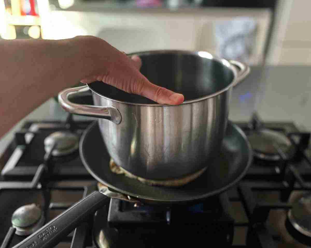 یک دست در حال فشار دادن یک قابلمه خالی است که روی یک آرایه در یک تابه داغ نشسته است.