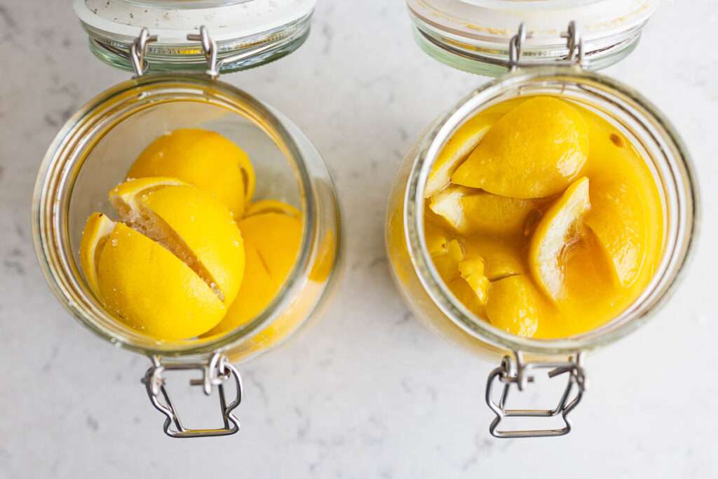 لیموهای نگهداری شده خانگی در شیشه های روی میز مرمر، از بالا، با لیموهای تازه در سمت چپ و لیموهای آماده در سمت راست